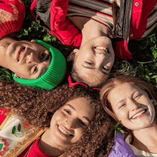 Portrait of young friends lying down on grass at public park - camera point of view

