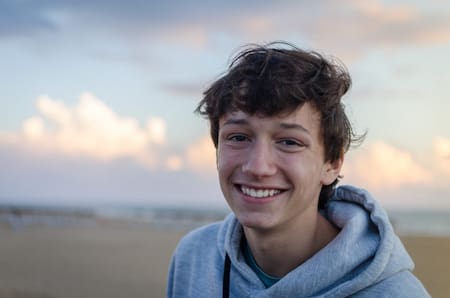 Portrait Of Smiling Teenage Boy At Beach Against Sky
